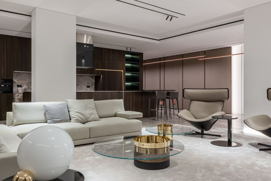 Comfortable armchairs and soft couch with cushions and small glass round table in modern studio apartment with kitchen and dining zone