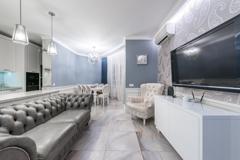 Modern light room with couch and TV on wall near armchair furnished with table and chairs next to cabinets